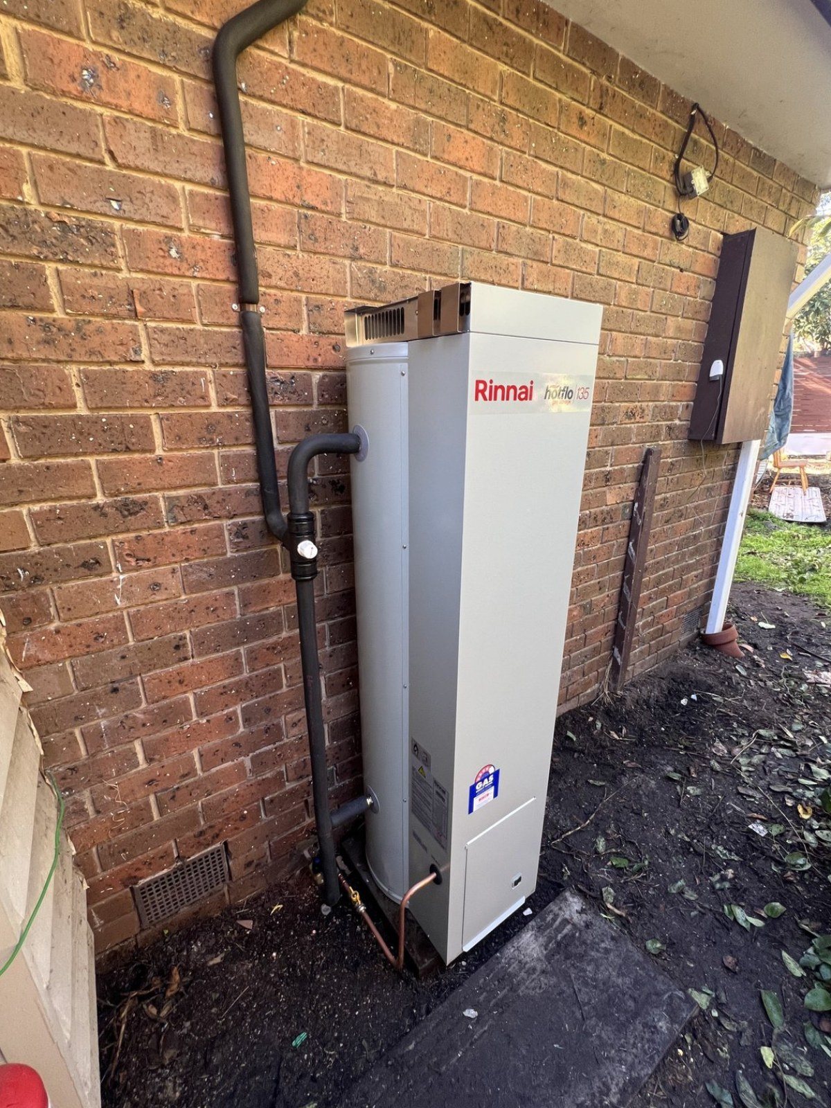 Gas storage hot water unit installed against a brick wall, with the relief drain line and copper at the base