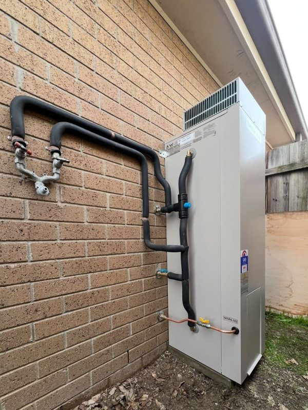 Storage hot water unit standing against a brick wall with lagged pipework running back into the wall